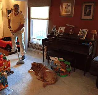 ABCO technician cleaning the carpet in a family living room while the dog rests nearby